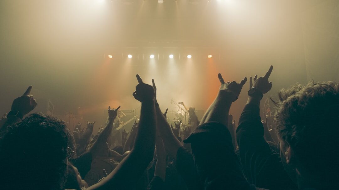Silhouettes of a crowd of fans raising their hands at a concert under bright stage light
